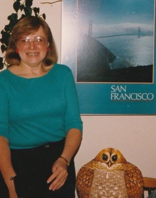 Woman smiling next to owl sculpture and poster.