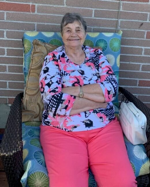 Elderly woman sitting on patio chair, smiling.