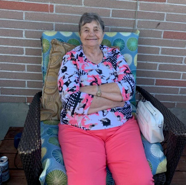 Elderly woman sitting on patio chair, smiling.