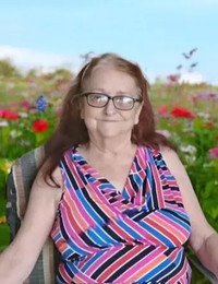 Smiling woman in colorful dress, seated outdoors.