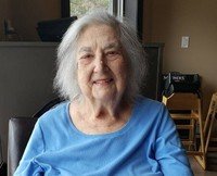 Elderly woman smiling indoors, wearing blue shirt.