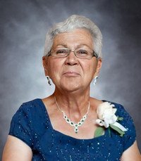 Elderly woman smiling in formal attire with flowers.