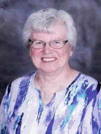 Smiling person in patterned blouse with gray background.