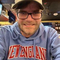 Smiling person wearing New England hoodie and cap.