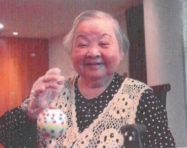 Elderly woman smiling, holding colorful ornament.