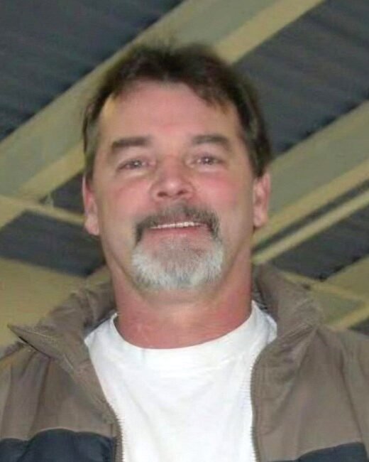 Man smiling indoors wearing a jacket and T-shirt.
