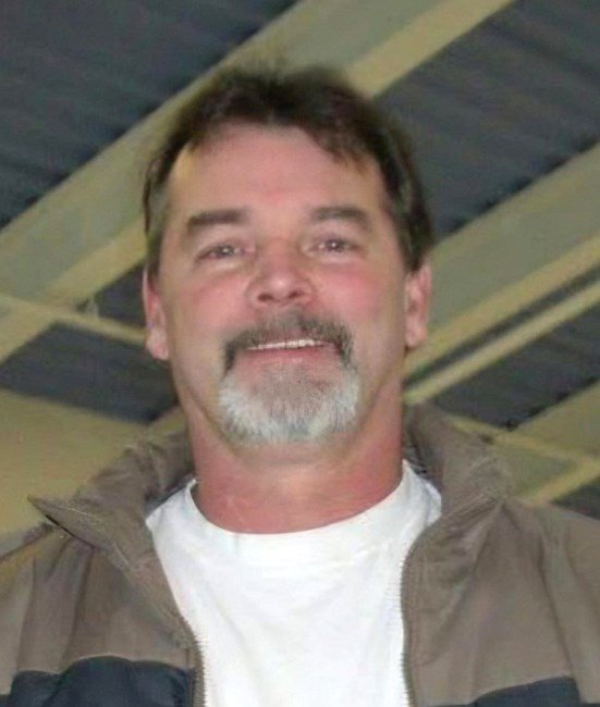 Man smiling indoors wearing a jacket and T-shirt.