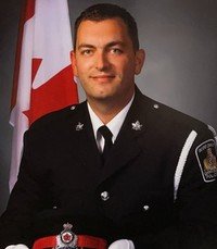 Uniformed officer in front of Canadian flag.