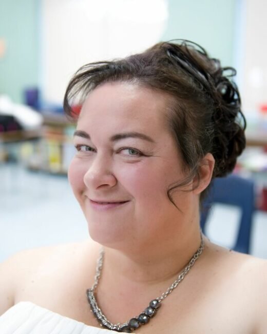 Smiling woman in a classroom setting, confident expression.