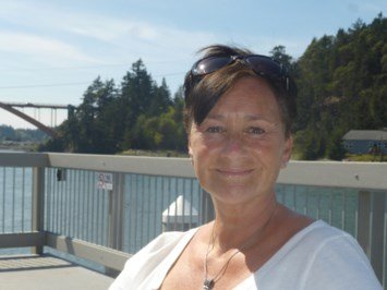 Smiling person outdoors by water and trees.