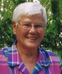 Smiling person with white hair and plaid shirt.