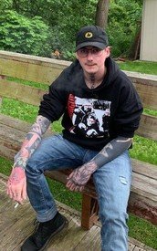 Person with tattoos sitting on wooden bench outdoors.