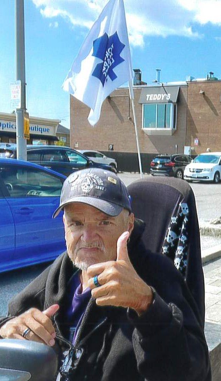 Man giving thumbs-up in urban setting with flag.
