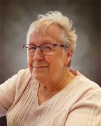 Elderly woman smiling, wearing glasses and a sweater.