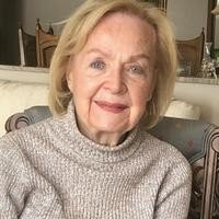 Elderly woman smiling in cozy sweater indoors.