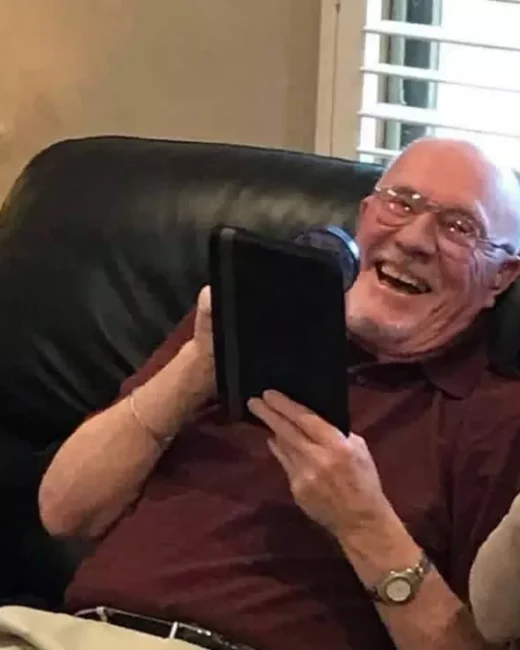 Elderly man laughing with iPad in hand.