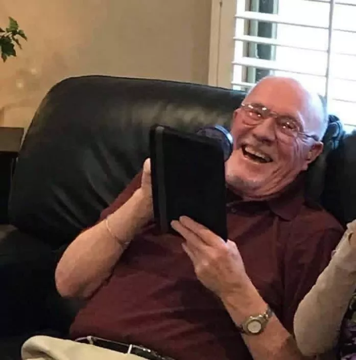 Elderly man laughing with iPad in hand.