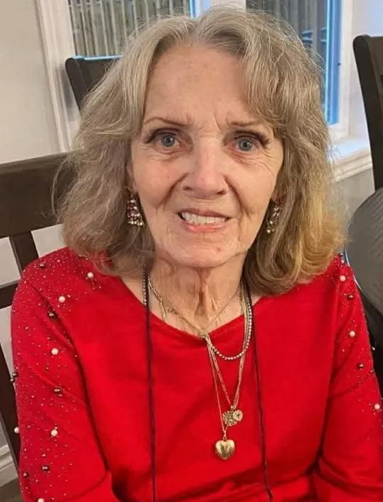 Elderly woman in red dress smiling indoors.