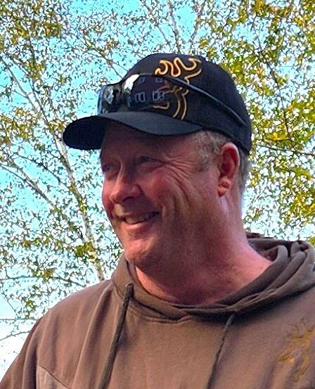 Smiling person outdoors wearing a cap and hoodie.