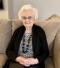 Elderly woman sitting on a couch, wearing glasses.