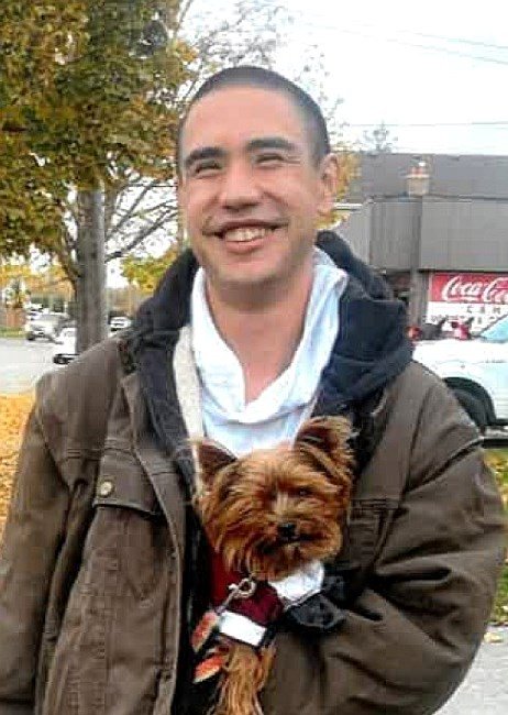Man smiling with small dog in jacket pocket.