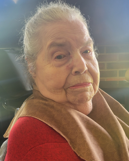Elderly woman with thoughtful expression and red attire.