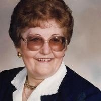 Elderly woman smiling in glasses and formal attire.