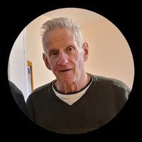 Older man with white hair, wearing a sweater.