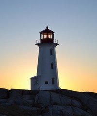 Lighthouse at sunset on rocky coastline.