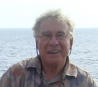 Person smiling by the ocean on a sunny day.