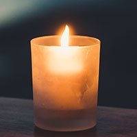 Lit candle in glass holder on wooden surface.