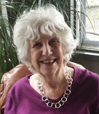 Smiling elderly woman with white hair and necklace.
