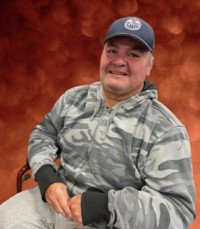 Smiling man in gray camo hoodie and cap.