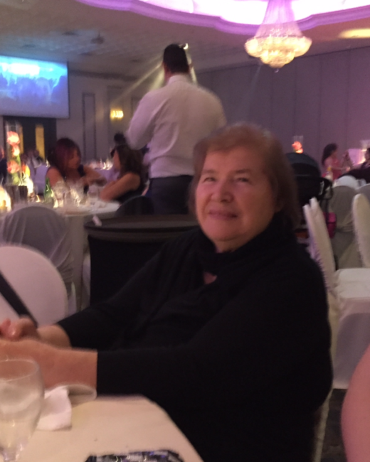 Elderly woman smiling at event with purple lighting.