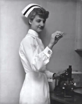 Nurse examining slide with microscope in laboratory.