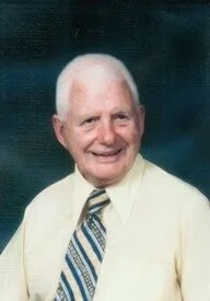 Elderly man smiling, wearing yellow shirt and tie.