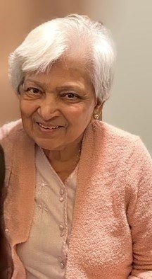 Smiling woman in pink cardigan, short white hair.