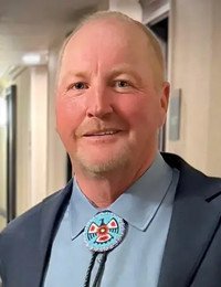 Person wearing a bolo tie and suit indoors.