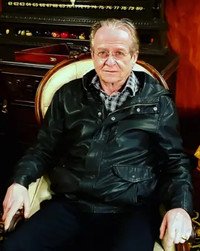Older man in leather jacket sitting indoors