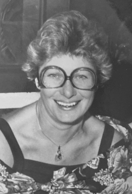 Smiling woman with glasses in floral dress.