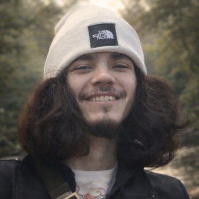 Smiling person wearing white beanie near trees