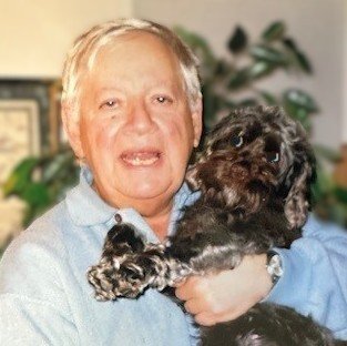 Man holding black dog indoors, smiling.