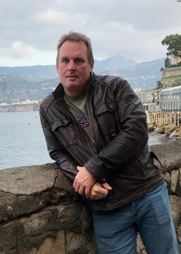 Man in leather jacket by a lake.