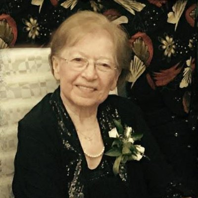 Elderly woman smiling, wearing floral attire.