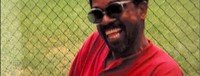 Smiling man in sunglasses near fence.
