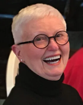 Person smiling with glasses and white hair