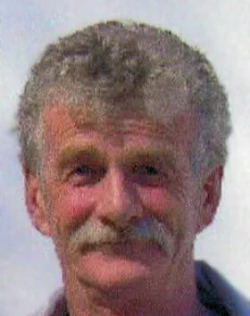Man with curly hair and mustache smiling slightly.
