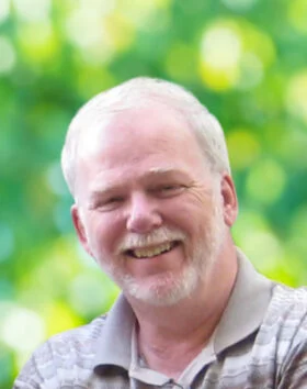 Smiling man outdoors with blurred green background.