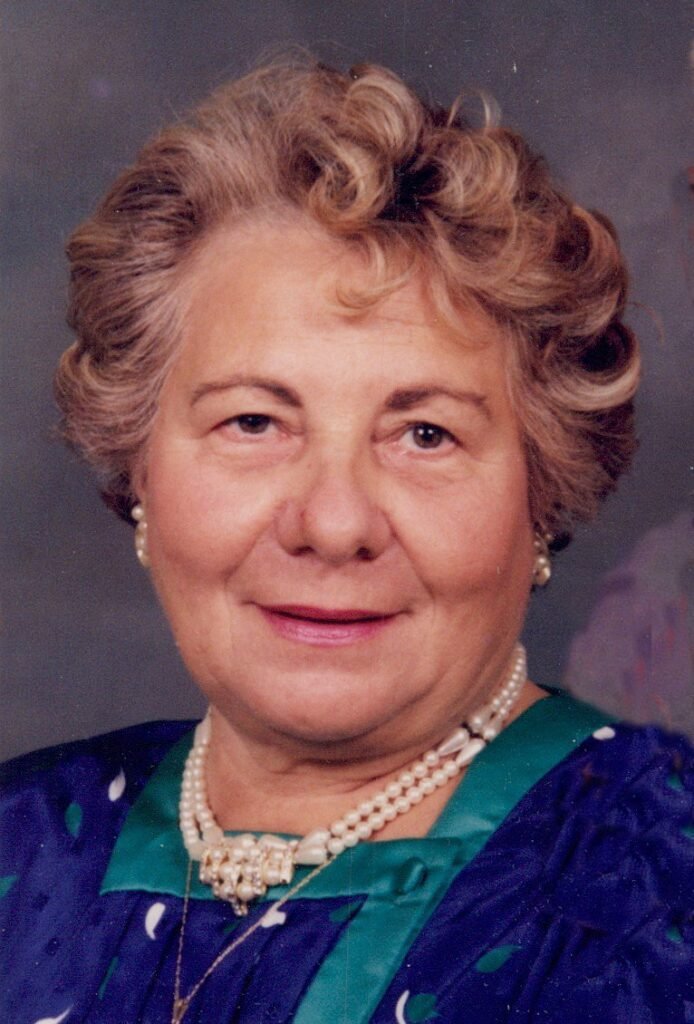Elderly woman wearing pearls, smiling.