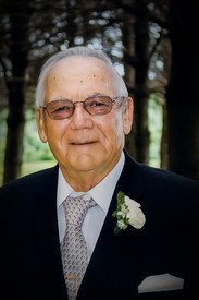 Elderly man in suit with glasses and boutonniere.